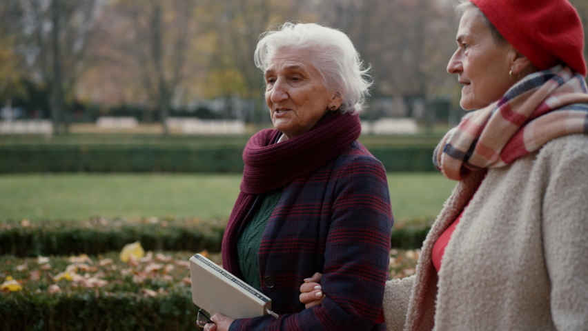 Happy senior women friends on walk outdoors in town park in autumn, looking at camera.