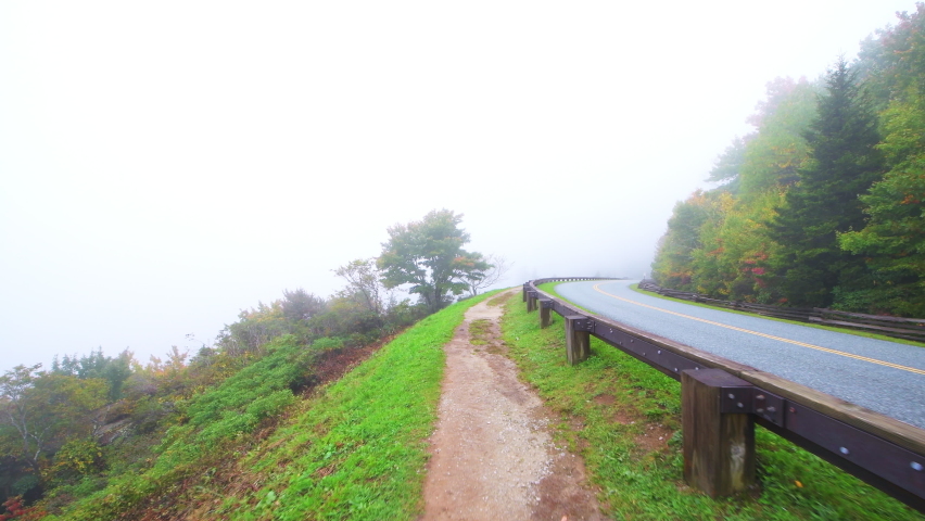 Point of view pov walking handheld shot by traffic guard rail barrier at Blue Ridge Parkway road, North Carolina at fall foliage mountains national park forest fog moody weather