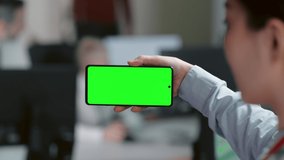 Female hand holding smartphone with green screen mockup up display. Female in formal clothes working in office and watching videos on mobile device 