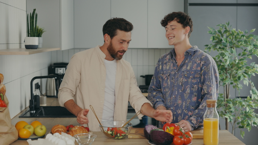 Lgbt couple in their new apartment in the kitchen enjoying cooking together. Two gay men make a salad. Romantic date, happy marriage, healthy eat concept