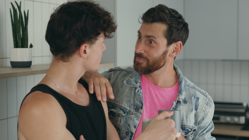 Close view of two happy guys feeling in love with each other standing drinking hot coffee in morning in their new apartment together. People and lgbt concept