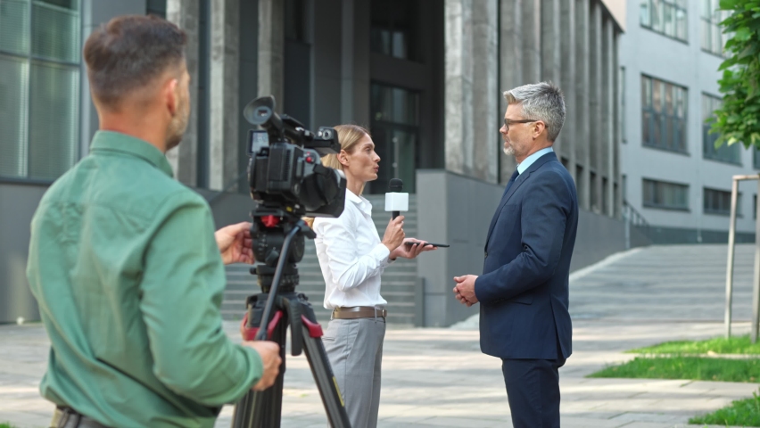 Caucasian beautiful woman TV correspondent holding smartphone and microphone interviewing middle-aged male politician standing in street. Handsome businessman talking on camera with female journalist Royalty-Free Stock Footage #1094171717
