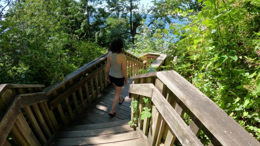 Woman Hiking Wooden Trail in the green forest with trees during sunny summer day. 1001 Steps in White Rock, Greater Vancouver, British Columbia, Canada.