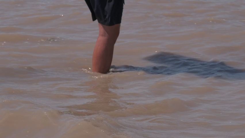 Man wearing swimming shirts and carring wakeboard is walking in the dirty water flow