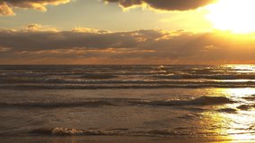 Scene of a beautiful sunset over the sea, the sun is shining on the camera, the waves are breaking on the sandy beach, 4k live video