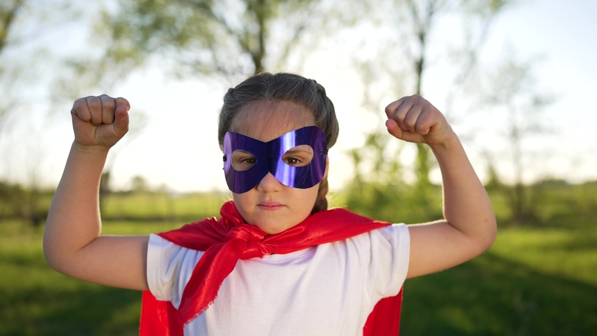 Happy girl dressed as superhero.Child play cheerfully with smile in park at sunset.Successful and brave kid in superhero mask.Girl with red cape on lawn in forest.Child winner success dream in park Royalty-Free Stock Footage #1094180235
