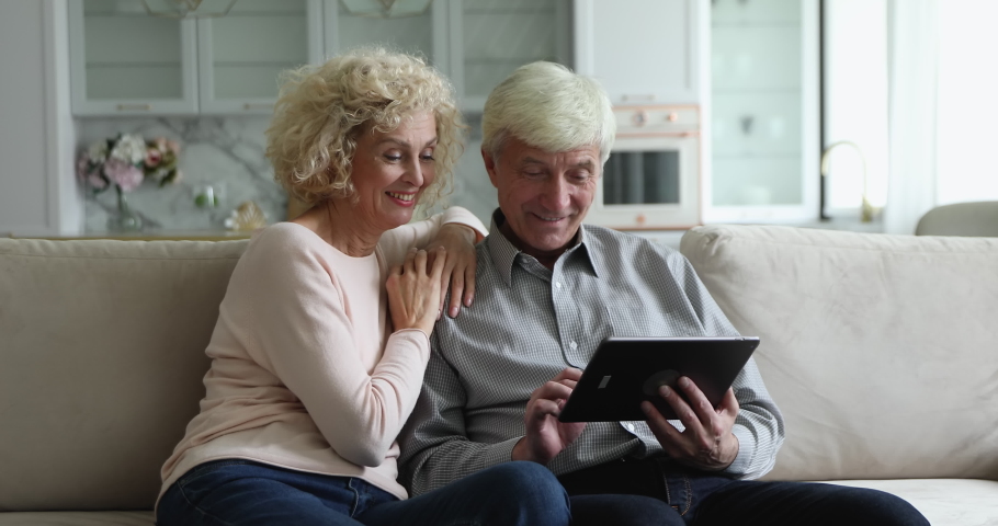 Cheerful elderly wife and grey haired husband using, discussing internet app on tablet computer, talking, laughing, smiling, shopping online, pointing at screen. Older age, modern technology concept Royalty-Free Stock Footage #1094184903