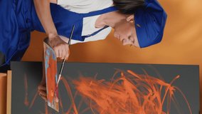 Vertical video: Mom and child learning to paint with orange aquarelle color and paintbrush, creating artwork design together on canvas. Happy people painting masterpiece with watercolor and brush.