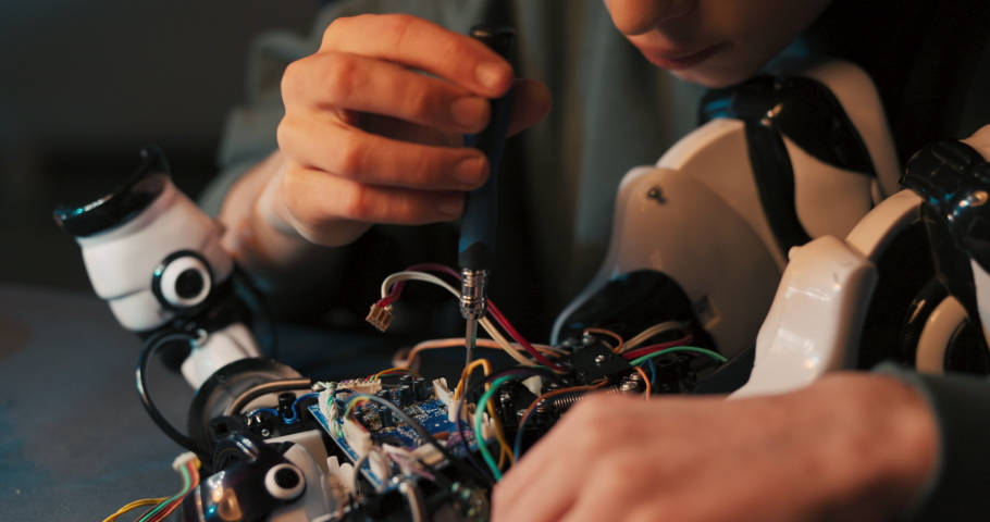 A portrait of a smiling boy, the talented intelligent student prepares a robot for the school competition, twists screws, assembles a toy from scratch.
