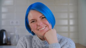 Portrait of blue haired female person looking in camera with a cheerful smile. Young white woman with dyed hair posing for video
