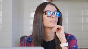 Pensive white woman in glasses thinking in front of computer. Pondering female looking away. Young Caucasian person in eyeglasses trying to solve problem and thinking about solution