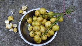A bunch of yellow ripe sour sweet latkan (Baccaurea motleyana) fruits in a steel bowl. Close up 4k video.