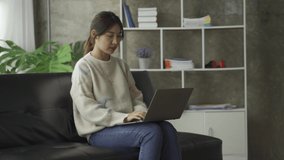 Asian woman sitting on sofa at home working on laptop educational concept 4k video