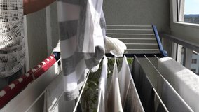 Woman hanging wet clean cloth on laundry drying rack in balkony at home. Close up of female hands hanging washed clothes, towels, linens on clothes wire dryer