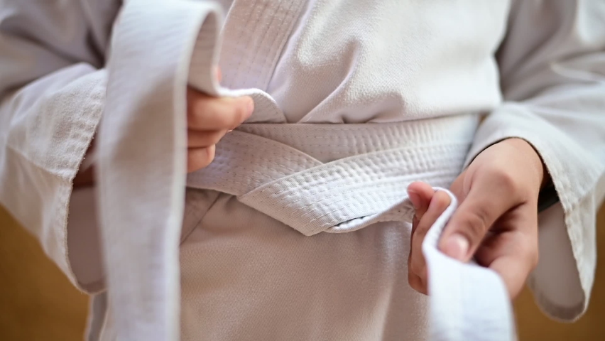 Karate fighter tightens or ties the white belt on her kimono before training. Slow-motion video. Royalty-Free Stock Footage #1094202793