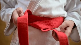 Karate fighter tightens or ties the orange belt on her kimono before training. Slow-motion video.