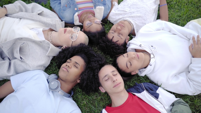 Boys and girls lying on grass with eyes closed, and them open eyes. They are tranquil and satisfied. Top view portrait