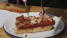 This close up video shows anonymous hands cutting a slice of gourmet pepperoni Detroit style pizza with a knife and fork.