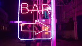 Beautiful young couple dancing and doing movement near bar neon sign lights . Neon bar sign medium shot . Night exterior video footage of vintage neon sign. Gimbal shot . Concept of nightlife .