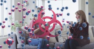 Animation of virus cells and biohazard symbol over caucasian female friends sitting on sofa. Global covid 19 pandemic, medicine and healthcare concept digitally generated video.