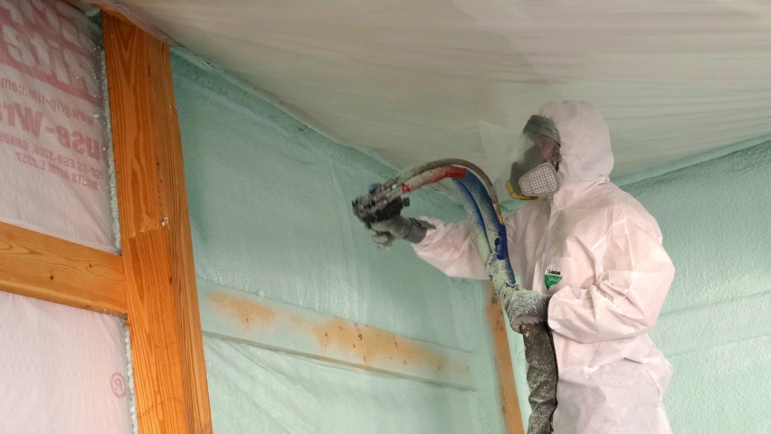 Worker in respirator and Tyvek suit sprays closed cell foam insulation near the ceiling of a newly constructed exterior wall; concepts of hazards, protection and new construction Royalty-Free Stock Footage #1094234559