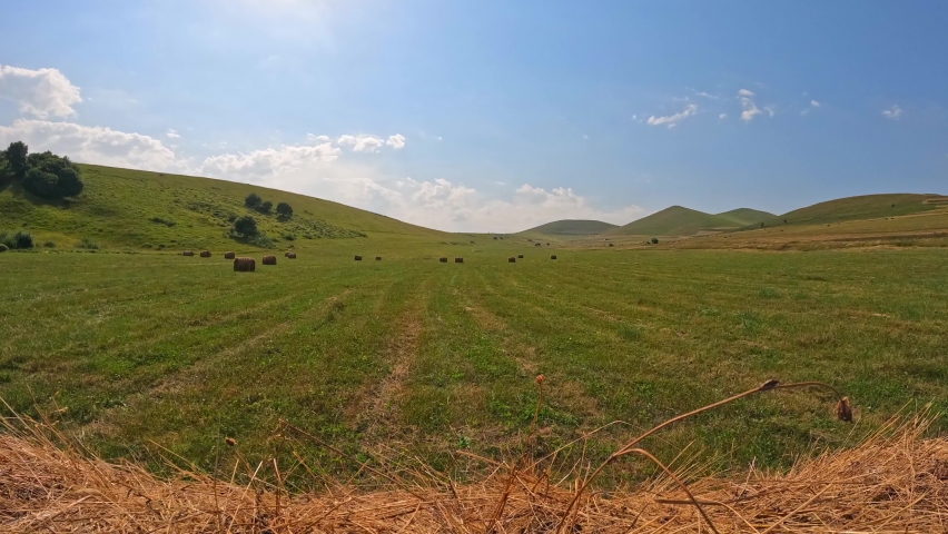 Timelapse view of a field with haystacks in a mountainous area, the clouds are moving in the blue sky