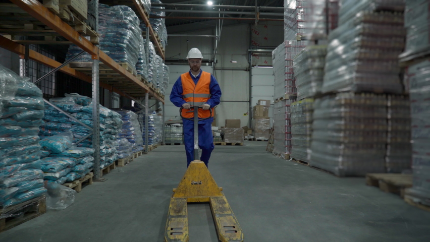 Worker Moves Pallet Jack Truck Equipment In Wares Storage Facility. Worker Uses Truck To Put Goods Into Storage At Industrial Warehouse. Storage Manager Worker In Hard Hat With Pallet Truck Tool - Powered by Shutterstock - Get 15% off with code: PIKWIZARD15