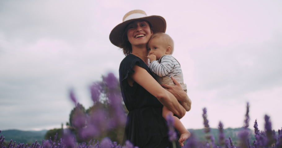 Happy Young Mom and her Beautiful little baby boy enjoying time together on lavender field in French Provence during sunset.