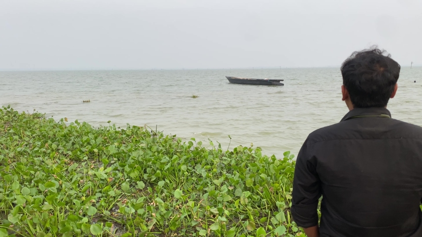 A man from the ghat of Kolkata is looking at the old wooden unmanned boat stuck in the sea 