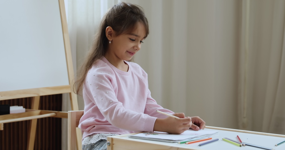 Happy little schoolkid girl drawing in coloring pencils in paper albums, sitting at small wooden studying desk, enjoying creative hobby, kindergarten activity in playroom. Preschool education concept Royalty-Free Stock Footage #1094244599