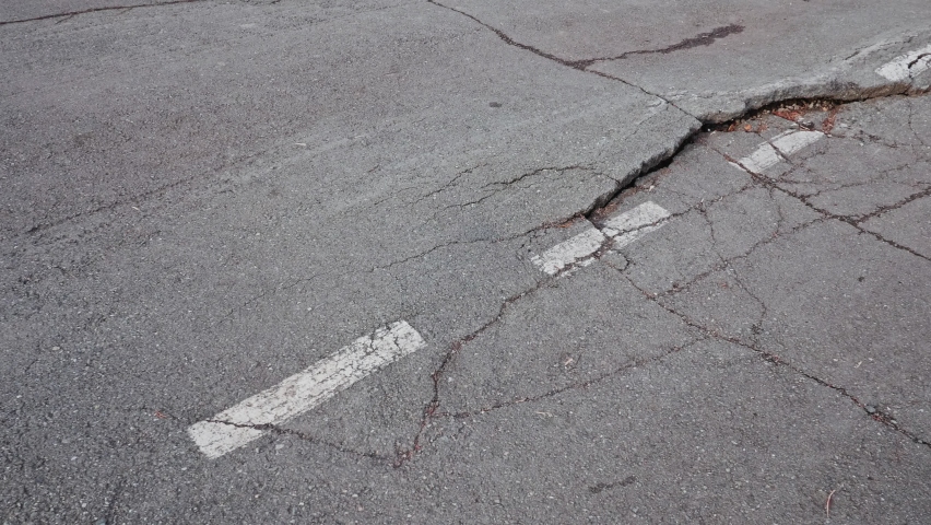 Crack with deep faults on the road next to the white road markings, destruction highway due to natural disaster or improper operation, tracking shot. Royalty-Free Stock Footage #1094244707