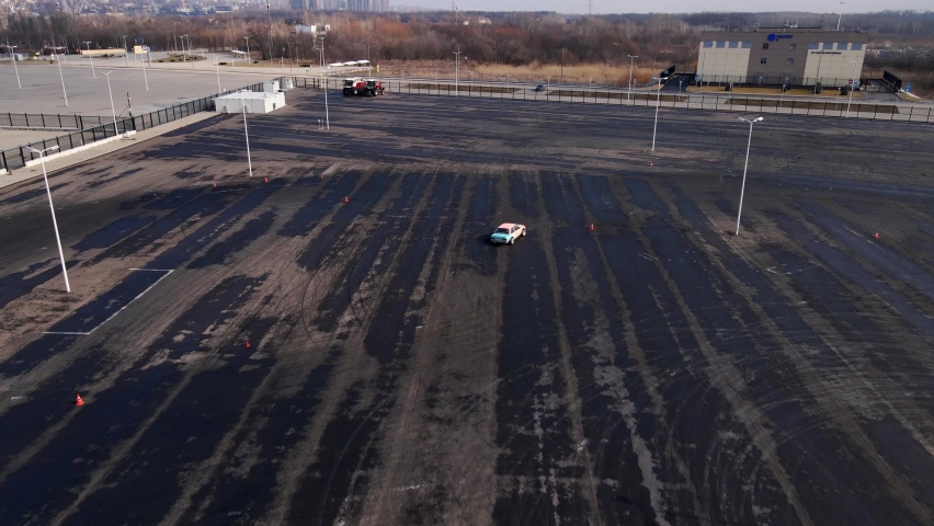Racing car drifts fast on asphalt platform in urban area. Repainted car makes sharp turns while going around street lights view from above