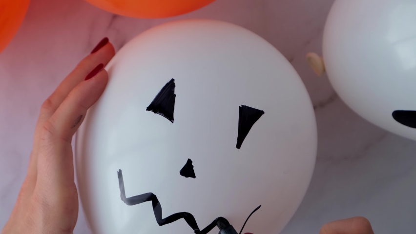 Female hands painting Jacks face on balloons. Orange and white balls preparation diy for halloween party. Halloween home activities. Handmade toys