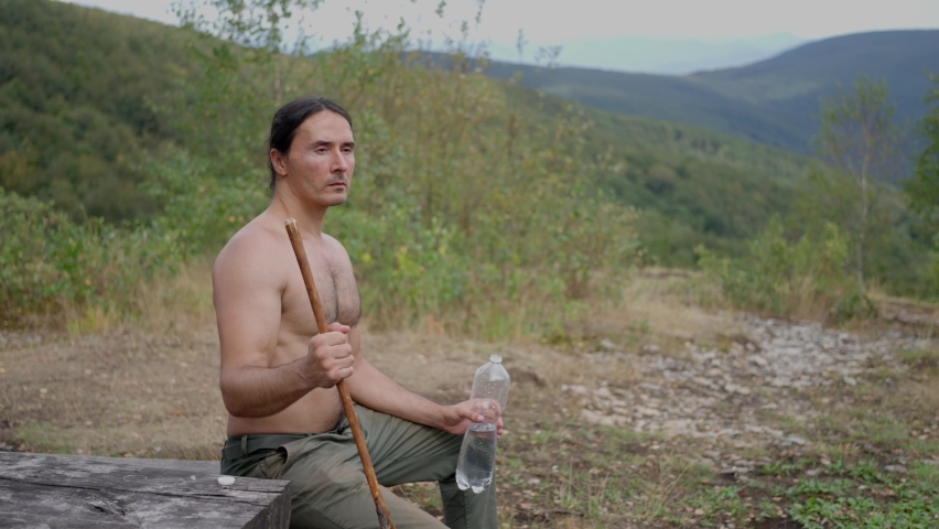 A tourist man, with long black hair, with a naked torso, sits on a wooden bench 