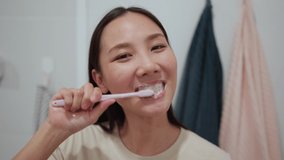 4K Happy Asian woman brushing teeth and looking to the mirror in bathroom with smiling. Attractive girl using toothbrush with whitening toothpaste cleaning teeth in the morning. Dental care concept. - Powered by Shutterstock - Get 15% off with code: PIKWIZARD15