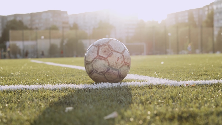 Old shabby training soccer ball lies on the artificial green grass of football pitch near corner of white lines in sunlight. Smooth stabilized camera approach to sports equipment. | Shutterstock HD Video #1094255095