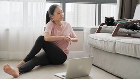 Young attractive Asian woman in sportswear learning workout exercise by watching exercise tutorials online class on laptop computer in living room with black cat on couch at home. Home fitness concept