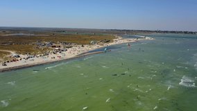 Aerial of many kiteboarders with colorful kites flying over the blue sea lagoon ride on kiteboards. Kitesurfers surf on waves with parachutes on windy day. Drone video.