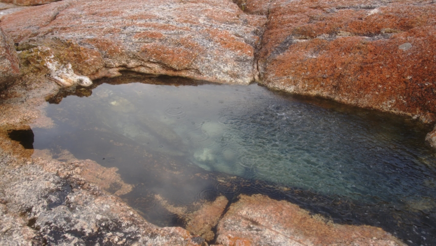 Ripples move across small red rock pool before dissipating to calm once again