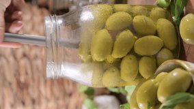 Large green olives in a cup on a wooden table. Italian olives, Sardenya and Greece harvest, olive leaves in the frame. close-up. Olive berries in a large jar and stacked separately. Vertical video