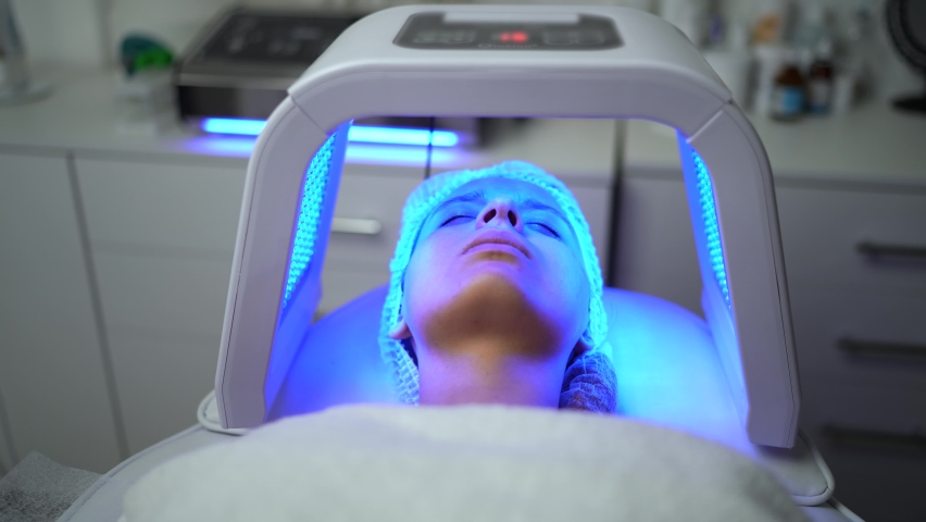 Close up of young woman having red and blue LED light facial therapy treatment in beauty salon. Woman laying on a couch and relaxing while LED light session. Beauty, healthcare and wellness concept. | Shutterstock HD Video #1094272017