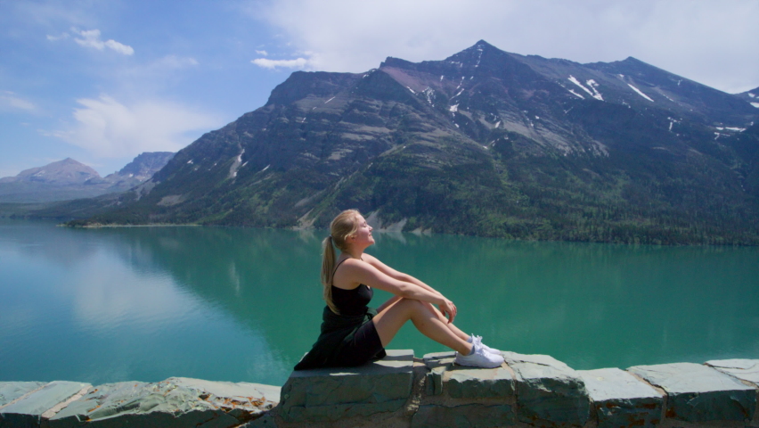 Beautiful woman enjoying the sunshine at Glacier National Park. Female traveler exploring pristine wilderness of epic natural landscape and panoramic views of mountain ranges. High quality 4k footage