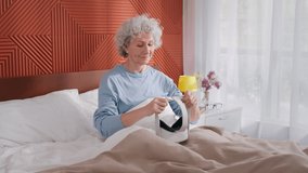 Senior woman in pajama wearing vr glasses headset goggles using 360 3d technology in bed. Grandmother in virtual reality headset use ar interface relaxing in morning in bedroom at home. 