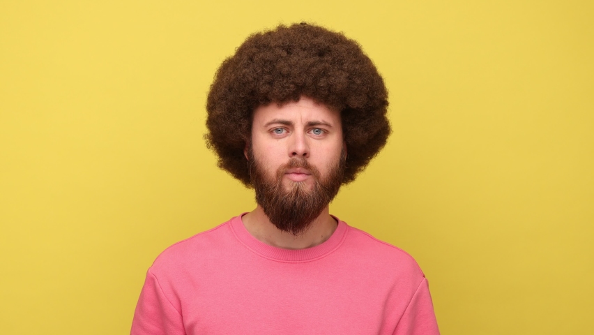Man with Afro hairstyle making fish face with pout lips and funny childish expression looking at camera with toothy smile, wearing pink sweatshirt. Indoor studio shot isolated on yellow background.