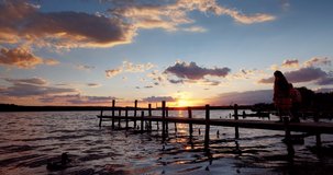 Boy and Girl Looking at the lake, enjoying dramatic sunset and walking on old wooden pier, 4k video