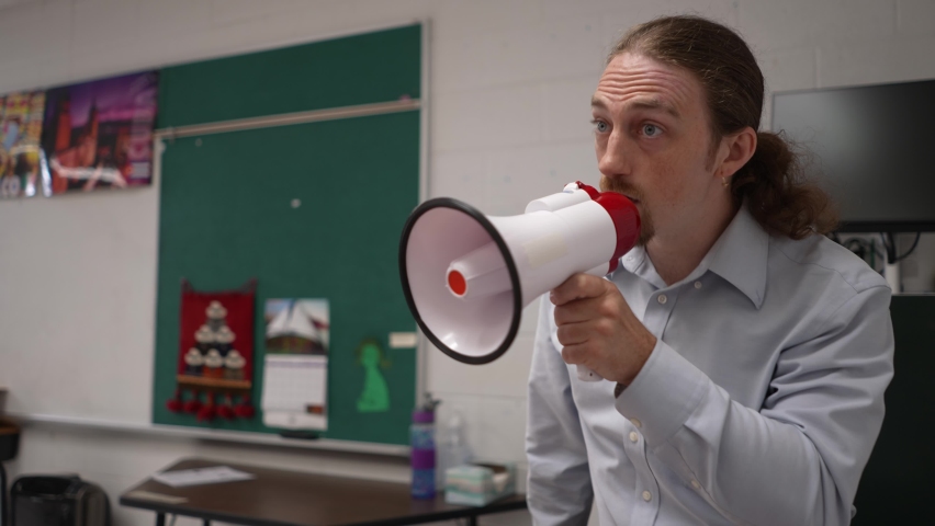 Angry teacher shouting in classroom into megaphone loudhailer, bullhorn, trying to make students listen. Concept of teacher frustration with class. Royalty-Free Stock Footage #1094289381