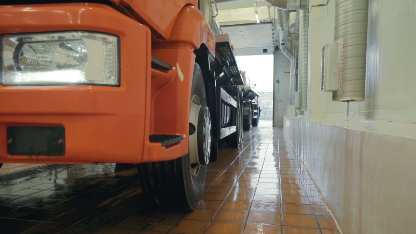 Milk transportation truck is exiting the manufacturing facility. Truck with multiple attached steel containers is transporting the dairy product. Transportation truck is reversing out of the factory.