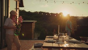 Everything is ready for family gathering. Senior woman arranging dining table with vase with flowers while her son barbecuing near her - Powered by Shutterstock - Get 15% off with code: PIKWIZARD15