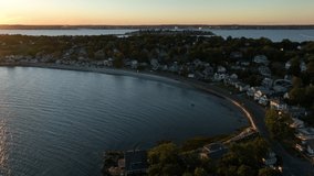 Aerial drone footage of Nahant, Massachusetts near Boston. Beautiful pink sky sunset on the Atlantic Ocean during summer. Waves on the rocky shoreline and boston cityscape in the distance.