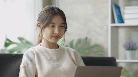 Beautiful young Asian woman college student is video call using laptop, smiling faces on sofa at home.